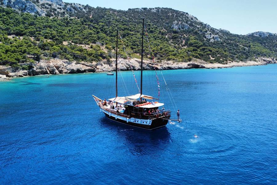 Agistri Aegina cruise gulet with swimmers off a pine-covered island in the deep blue Saronic Gulf