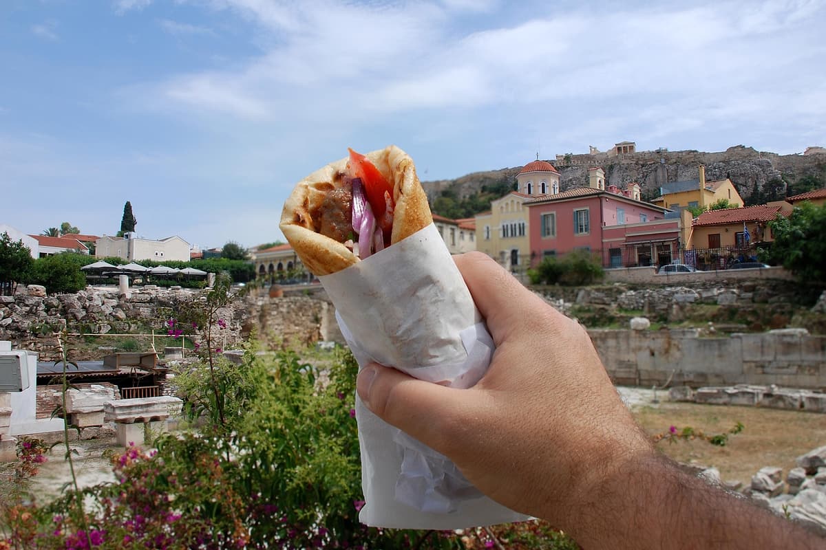 Athens food tour souvlaki pita held up over ancient ruins below Plaka and the Acropolis