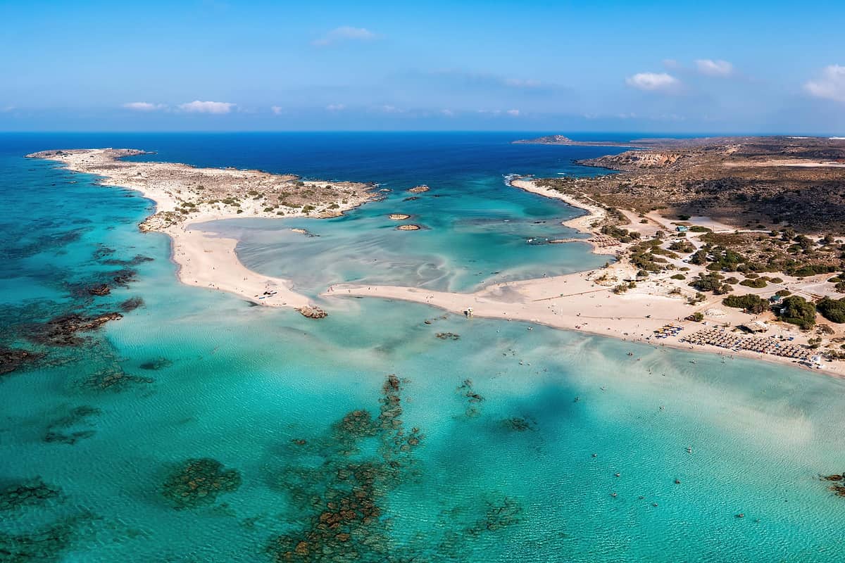 Elafonisi day trip seen from above: the islet, the shallow turquoise lagoon and visitors wading off the pink-edged beach
