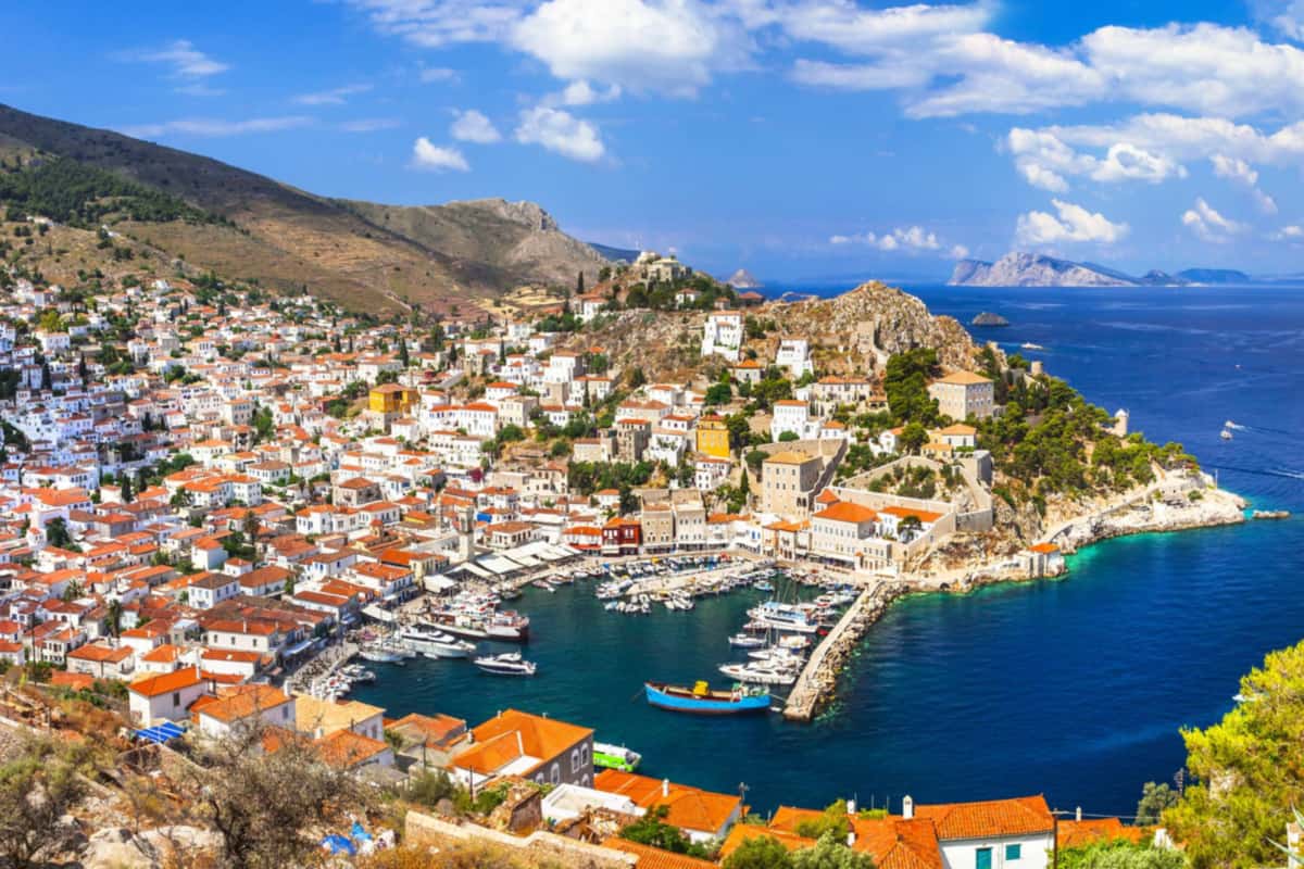 Hydra day trip view of Hydra town harbour from above, with stone mansions climbing the hillside around boats moored inside the stone mole