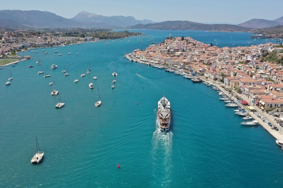 Hydra Poros Aegina cruise ship sailing through the turquoise Poros strait, with the red roofs of Poros town along the shore