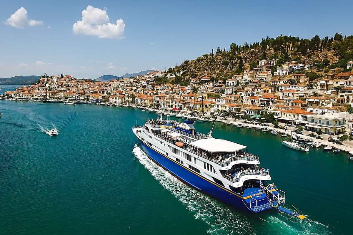 Hydra Poros Aegina cruise ship sailing into Poros town across turquoise water, with red-roofed houses on the hillside