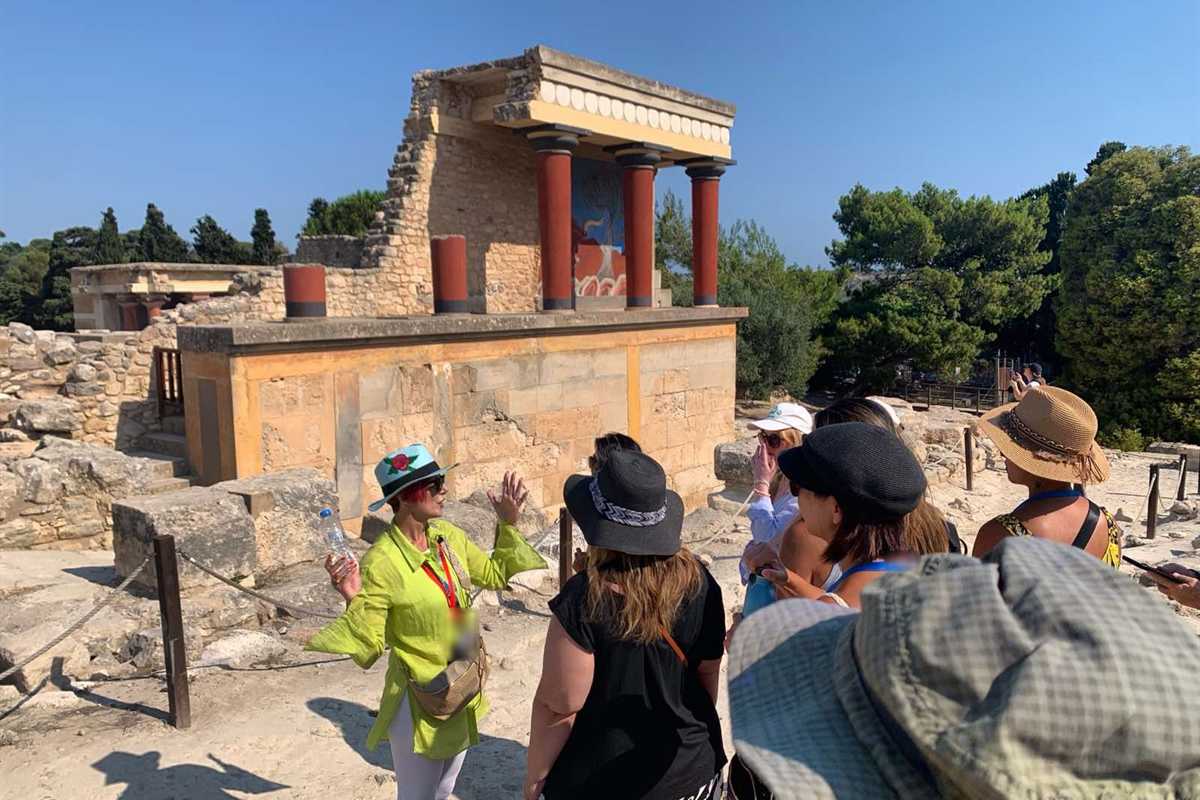 Tour leader explaining the North Entrance to a group on a Knossos palace tour, red columns and charging-bull fresco