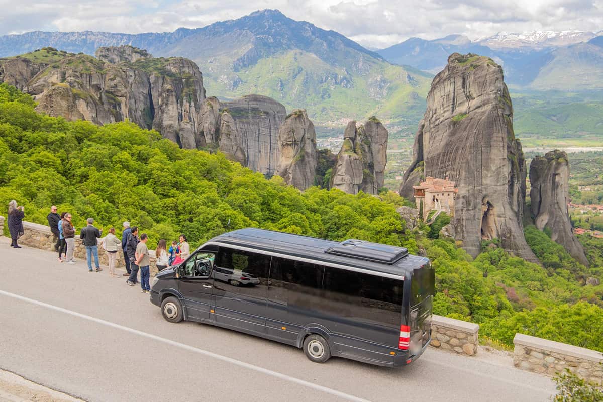 Tour group and minibus at a viewpoint above a monastery on its rock pillar on a Meteora day trip from Athens