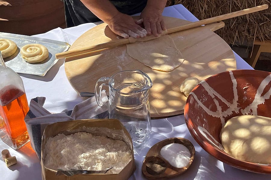 Naxos cooking class hands rolling out fresh dough on a wooden board beside flour and a clay bowl