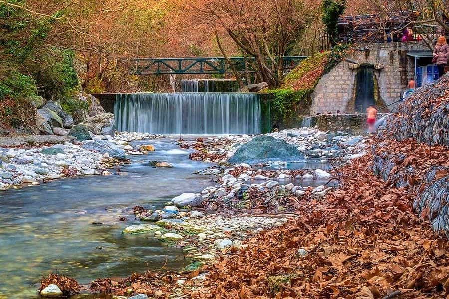 The thermal river at the Pozar thermal baths, flowing below the weir and footbridge in autumn