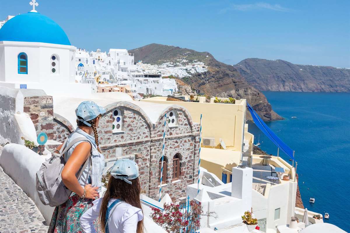 Two visitors on a Santorini private tour look over the Oia caldera from a whitewashed lane