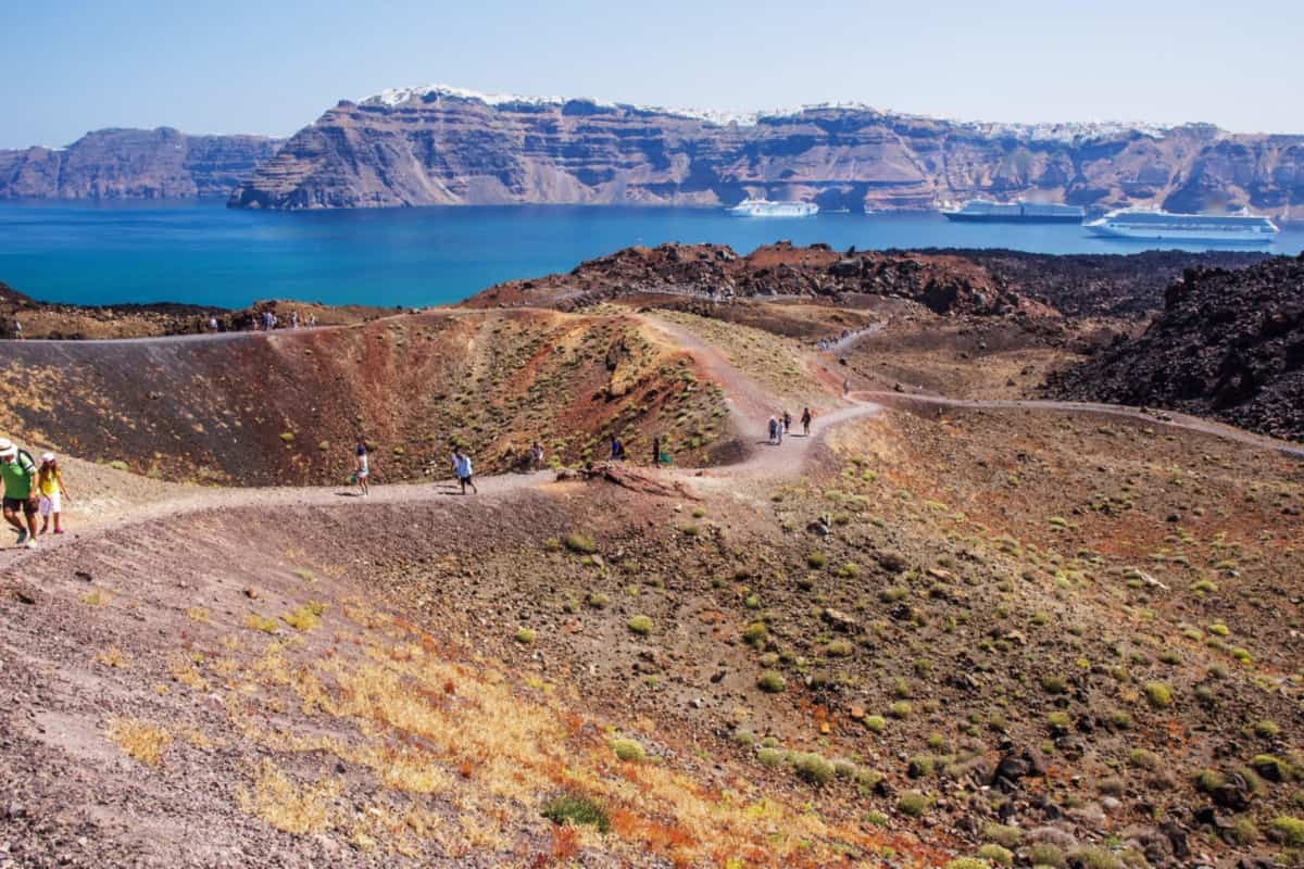 Santorini volcano tour hikers on the Nea Kameni crater path, with the caldera cliffs behind