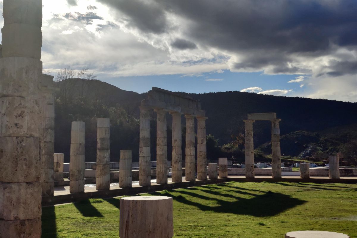 Vergina day trip: the restored stone columns of the Palace of Aigai stand on green grass under a cloudy sky with wooded hills behind.